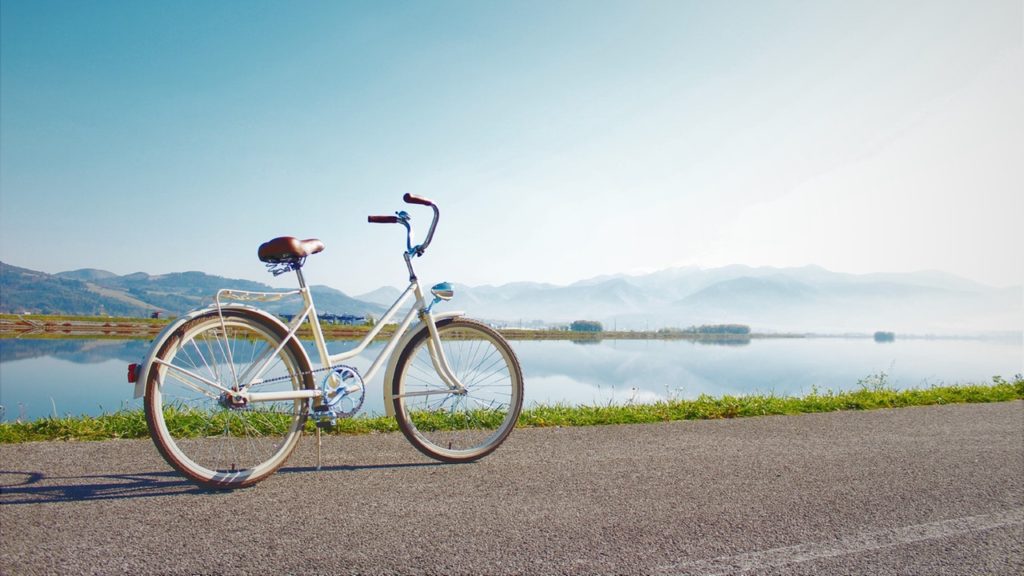 White bike on road in front of a lake and mountains