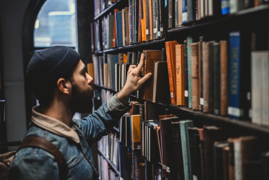 man fingering through books in library