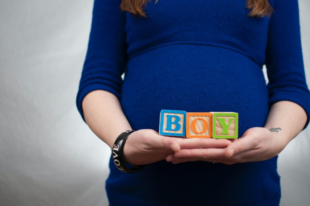 The belly of a pregnant woman expecting holding up blocks that read boy