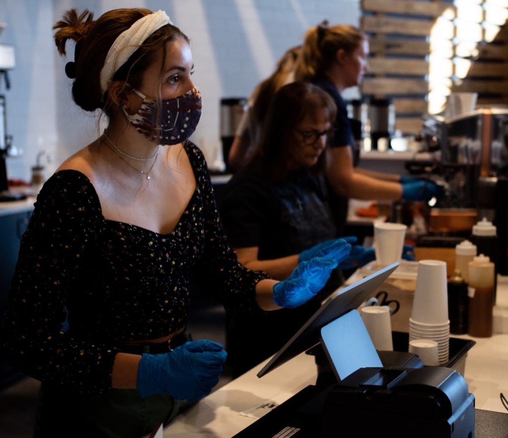 A girl in a mask and gloves at a register ringing customers up at a restaurant during Covid-19