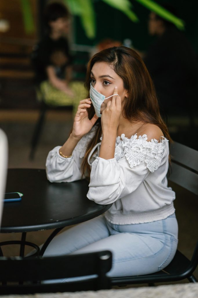 Girl sitting at a table on her cell phone taking off her paper mask