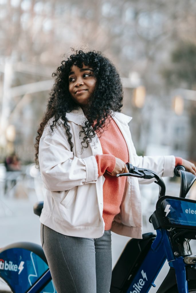 A girl in a light jacket looks over her shoulder with her bike