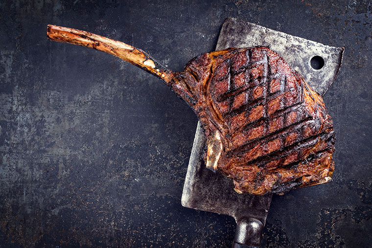 Tomahawk steak resting on butcher knife.