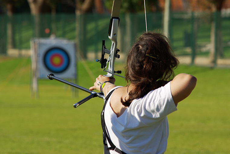 Woman aiming towards target with bow and arrow
