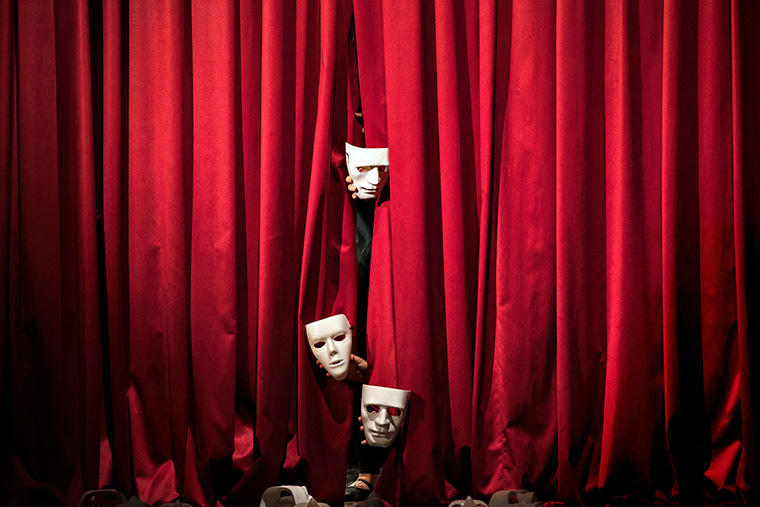 Red curtain adorned with three hands emerging from it, clutching masks representing various performing arts