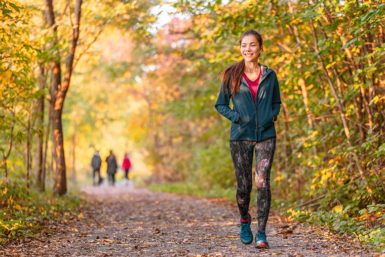 A joyous woman strolling along a nature trail, donned in cozy jogging attire designed to keep her warm.