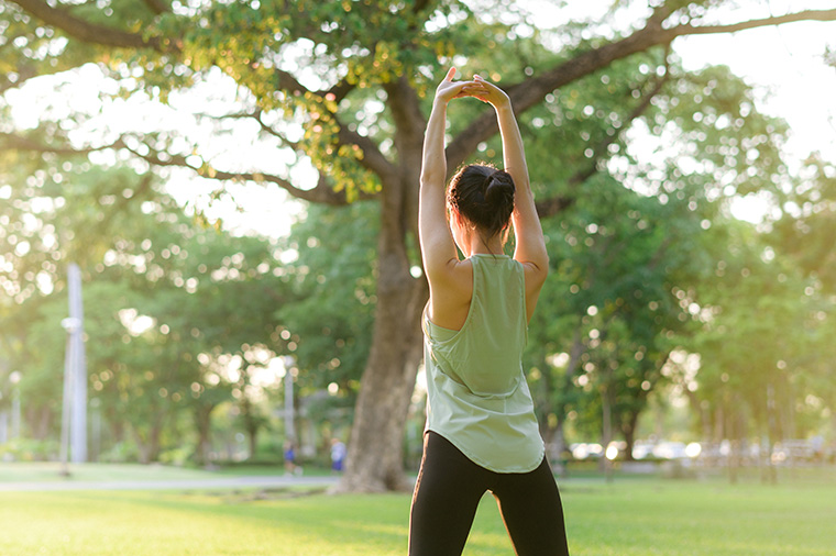 A calm lady finds peace in a quiet park while doing yoga, surrounded by nature's beauty.